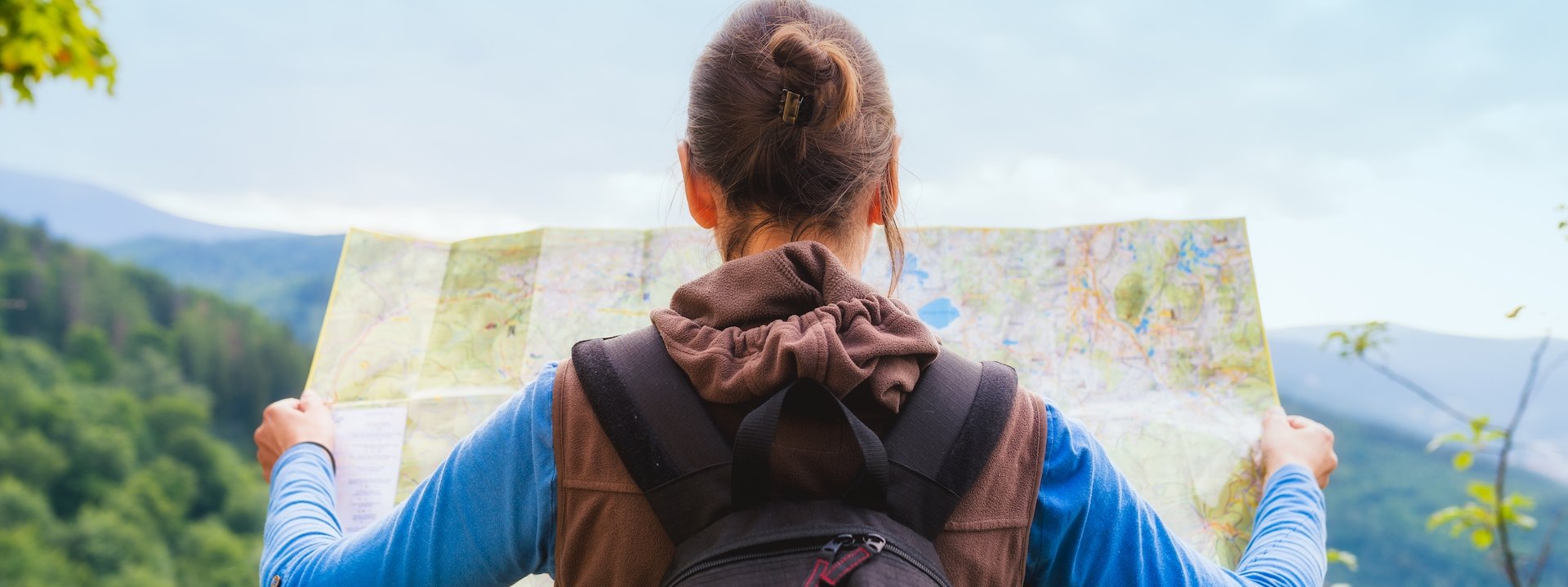Hiking woman traveler with backpack checks map to find directions in wilderness area, real explorer. Travel Concept