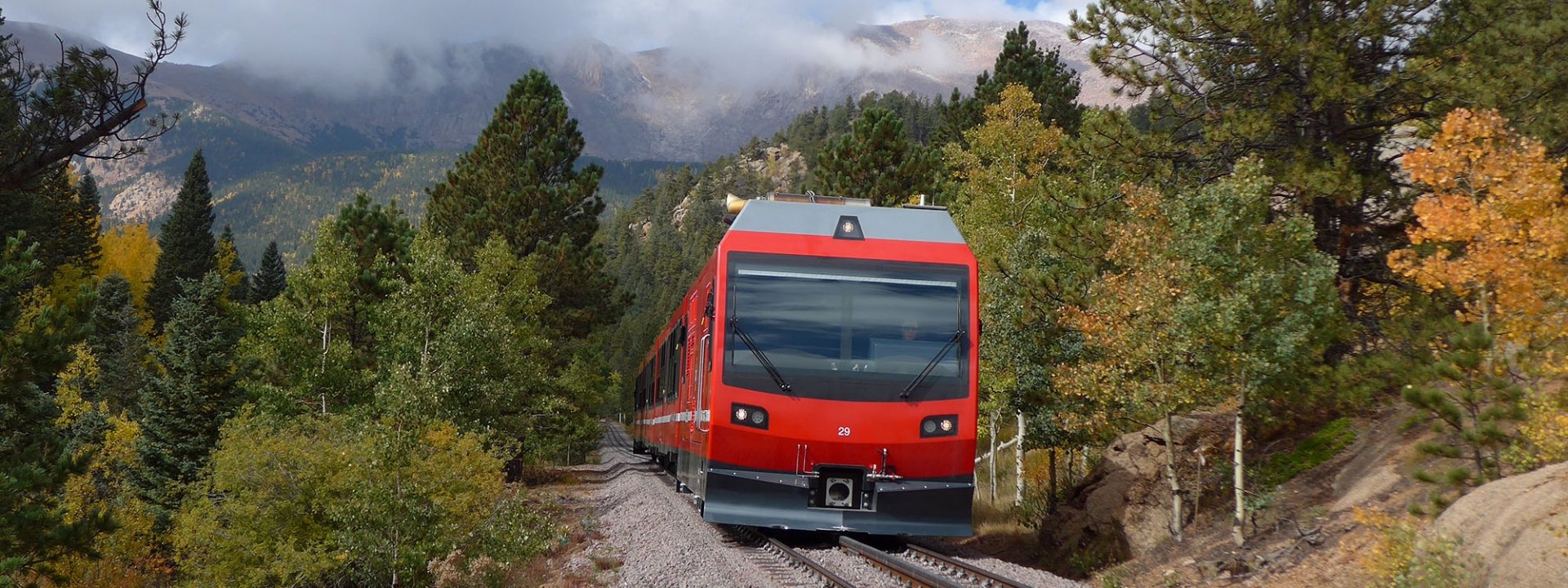 Red train on railway tracks with green and yellow trees in background