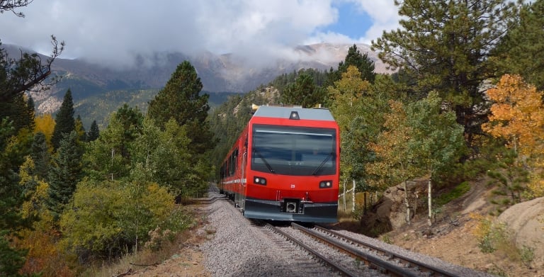 Red train on railway tracks with green and yellow trees in background