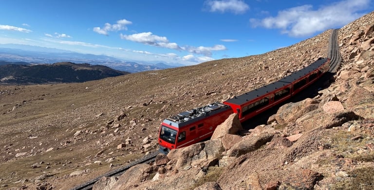 red train coming down mountain on sunny day
