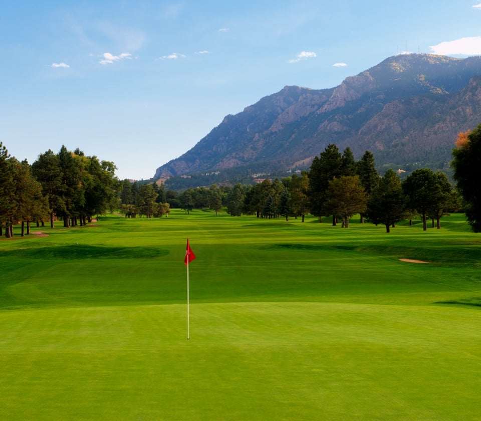 Golf green with red flagstick and mountains in background